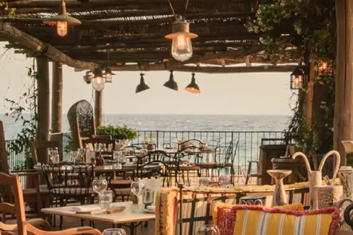 Terrace dining area with string lights and rustic pergola overlooking the sea at dusk