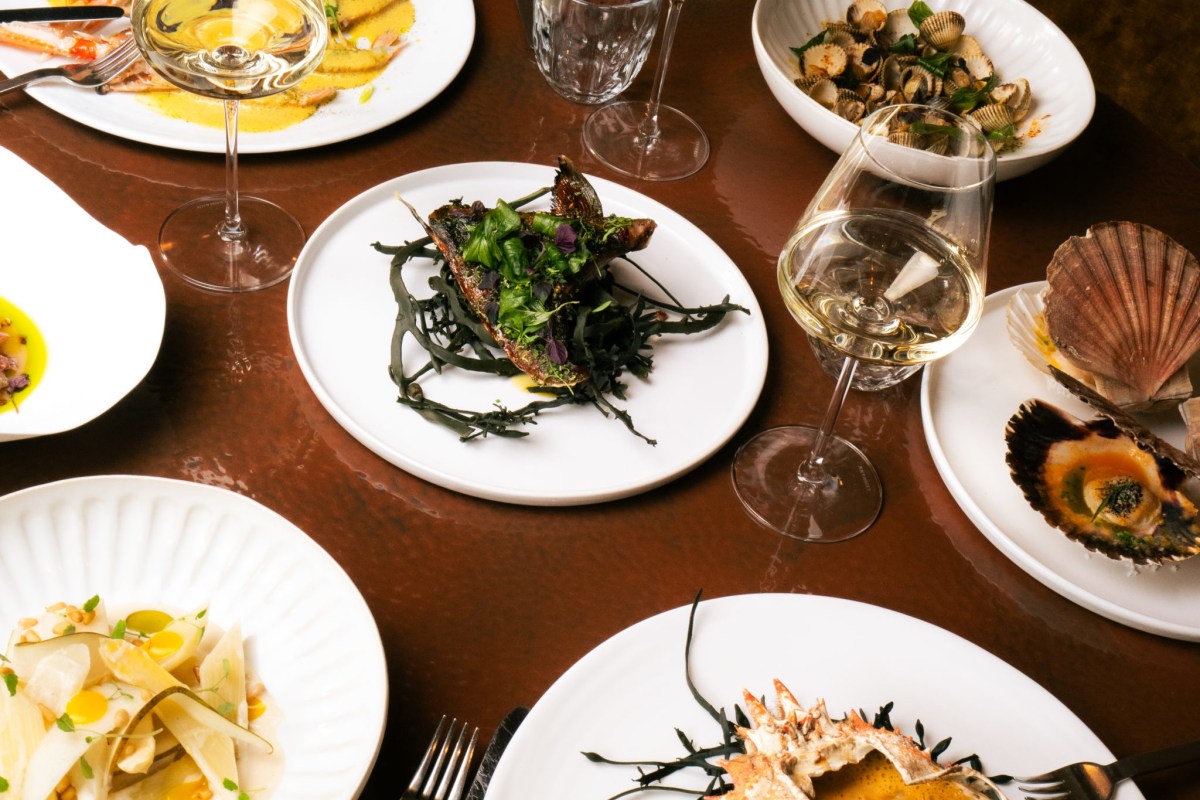 Overhead view of a restaurant table laid with seafood dishes, oysters, scallops, crab and white wine glasses