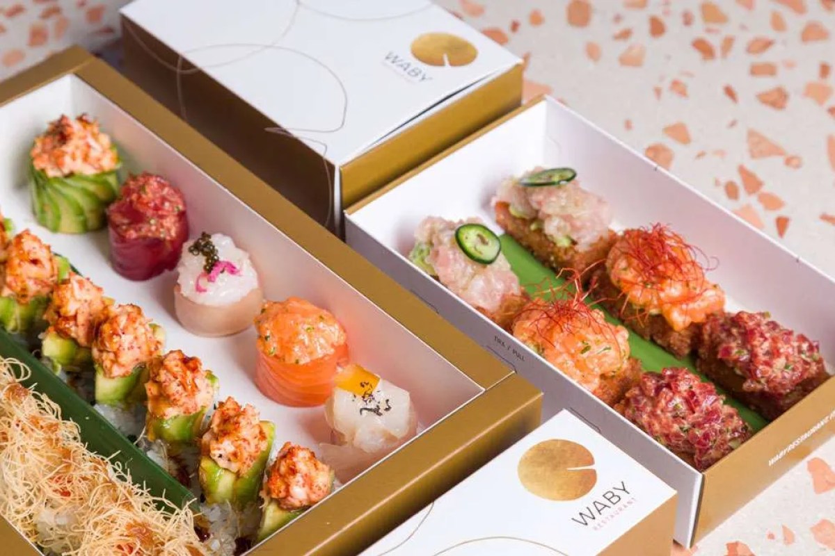 Two takeaway boxes with sushi rolls and sashimi branded with Waby restaurant logo