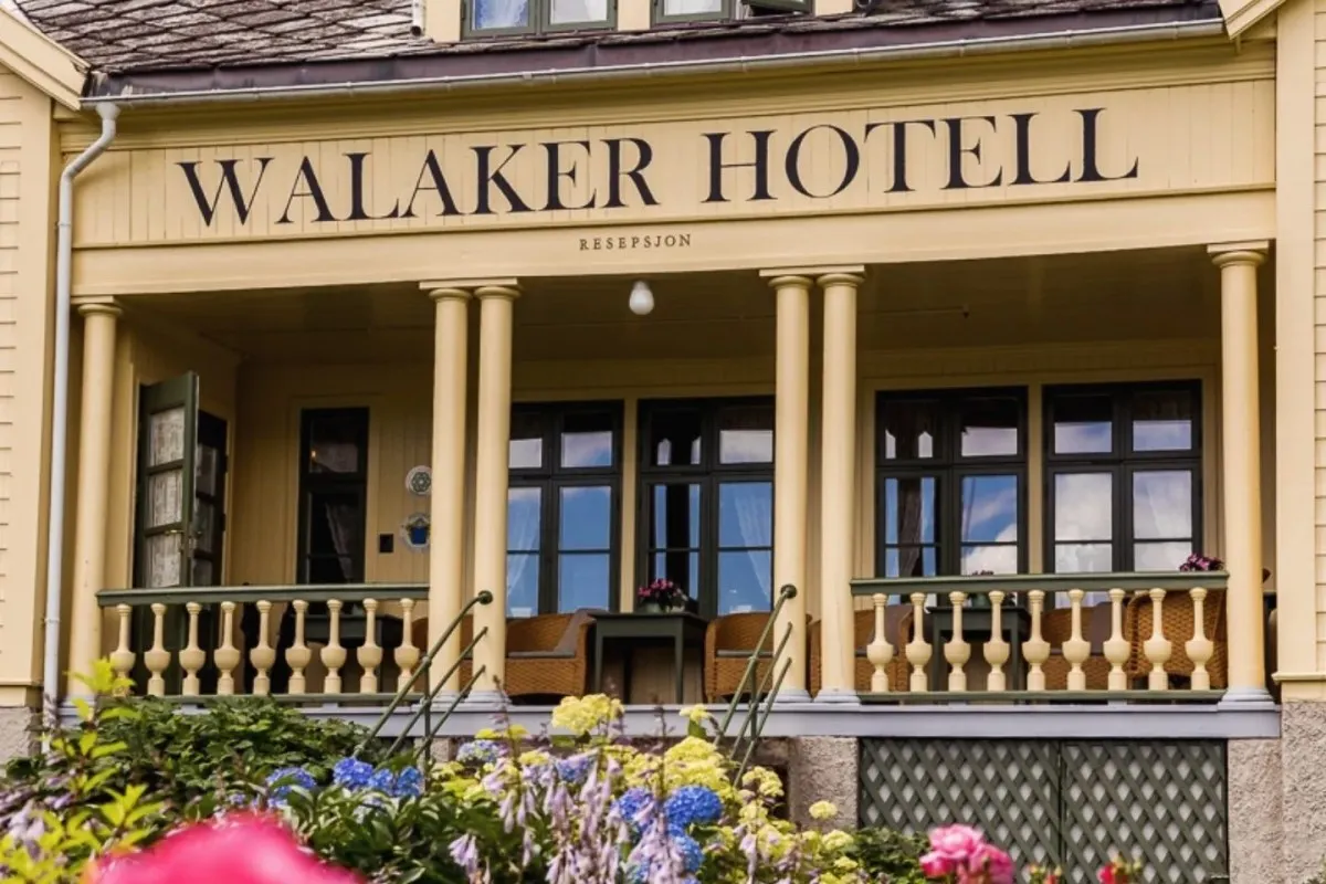 Close-up of the Walaker Hotell's yellow facade with columned porch, sign, and flowers in foreground
