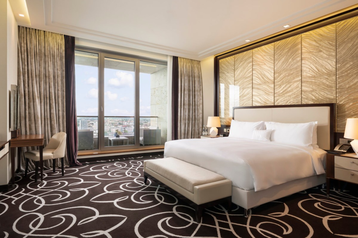 Modern hotel bedroom with white bed, patterned carpet and city view window