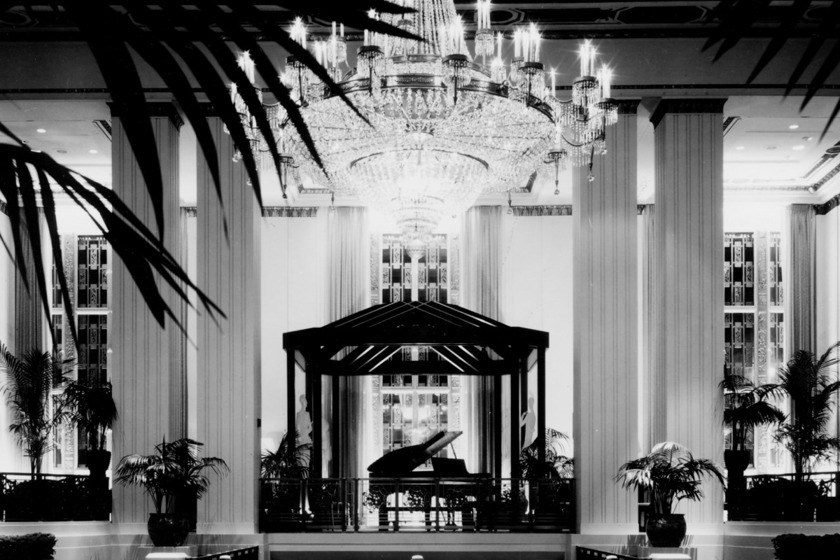 Grand Art Deco hotel lobby with crystal chandelier, tall columns and palm plants