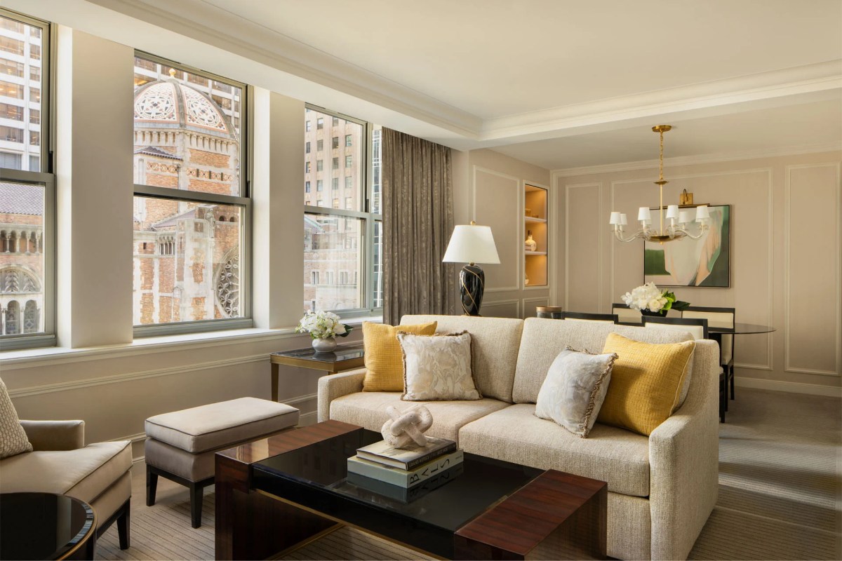Elegant hotel suite living room with beige sofa, yellow pillows and city view through large windows