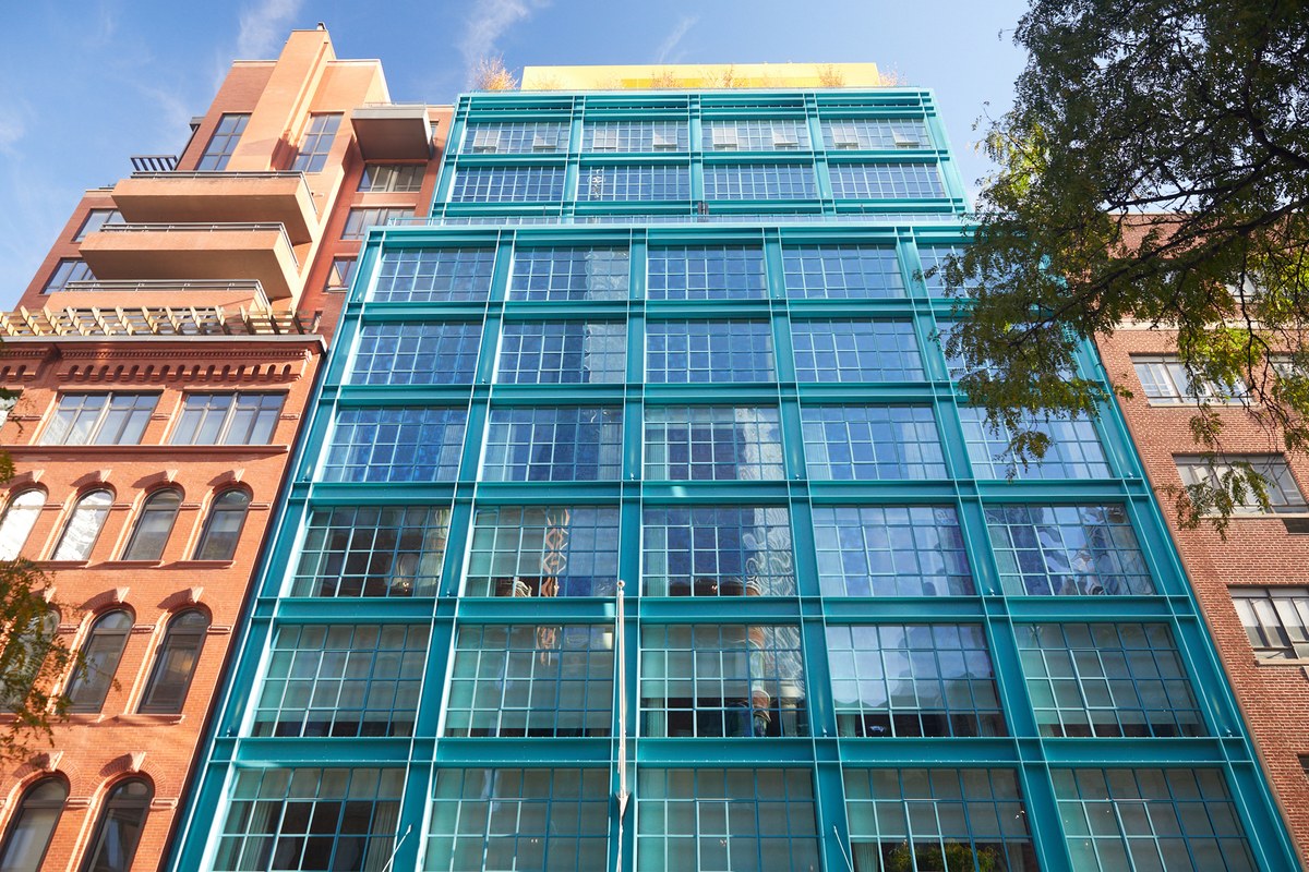 Upward view of the teal-framed glass façade of Warren Street Hotel between neighboring brick buildings in New York City