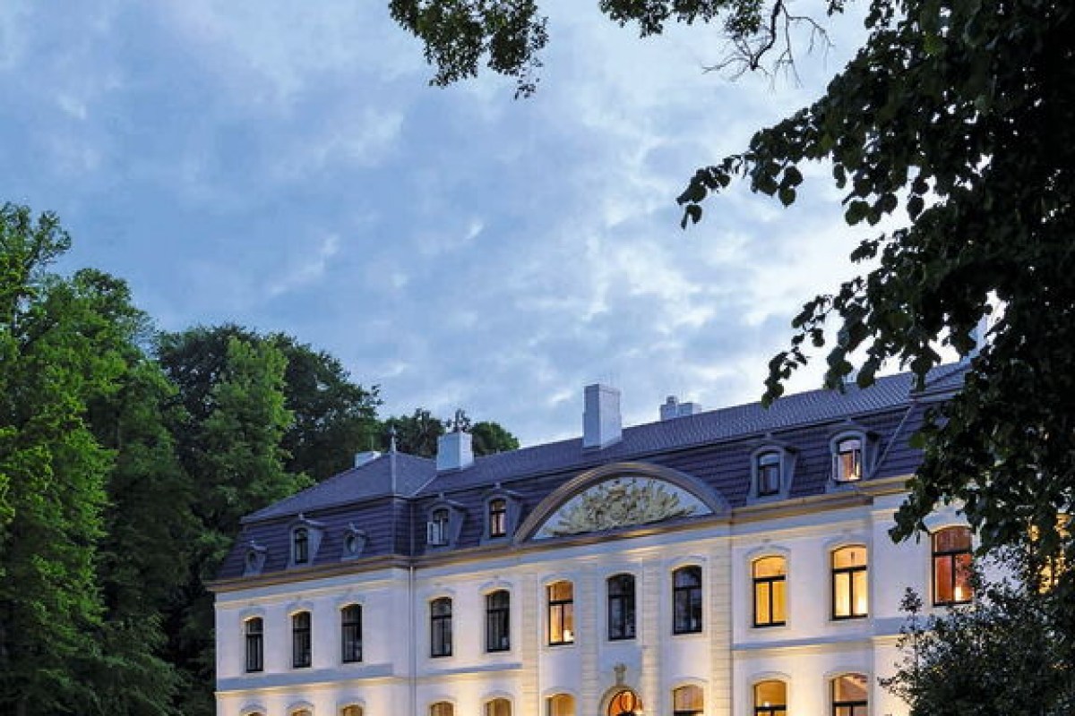 Illuminated historic manor house facade at dusk, surrounded by trees, main hotel building