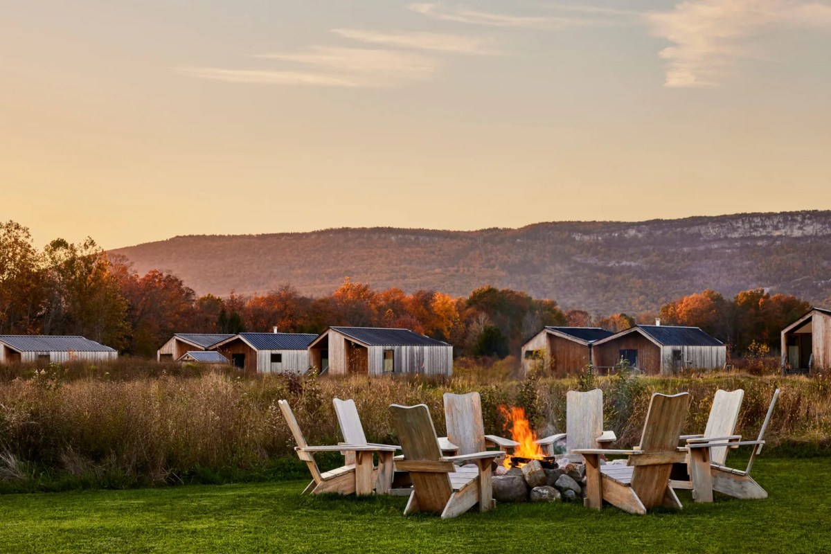 Wooden cabins at dusk with fire pit and Adirondack chairs, autumn foliage and mountains behind