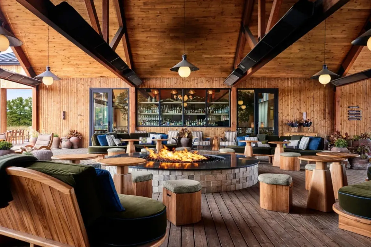 Wood-beamed lounge with central fire pit, bar, and cozy seating area at Wildflower Farms
