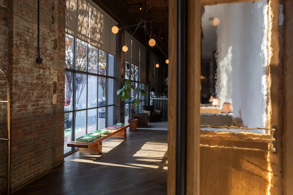 Hotel lobby with exposed brick, large windows, wood floors and bench with magazines