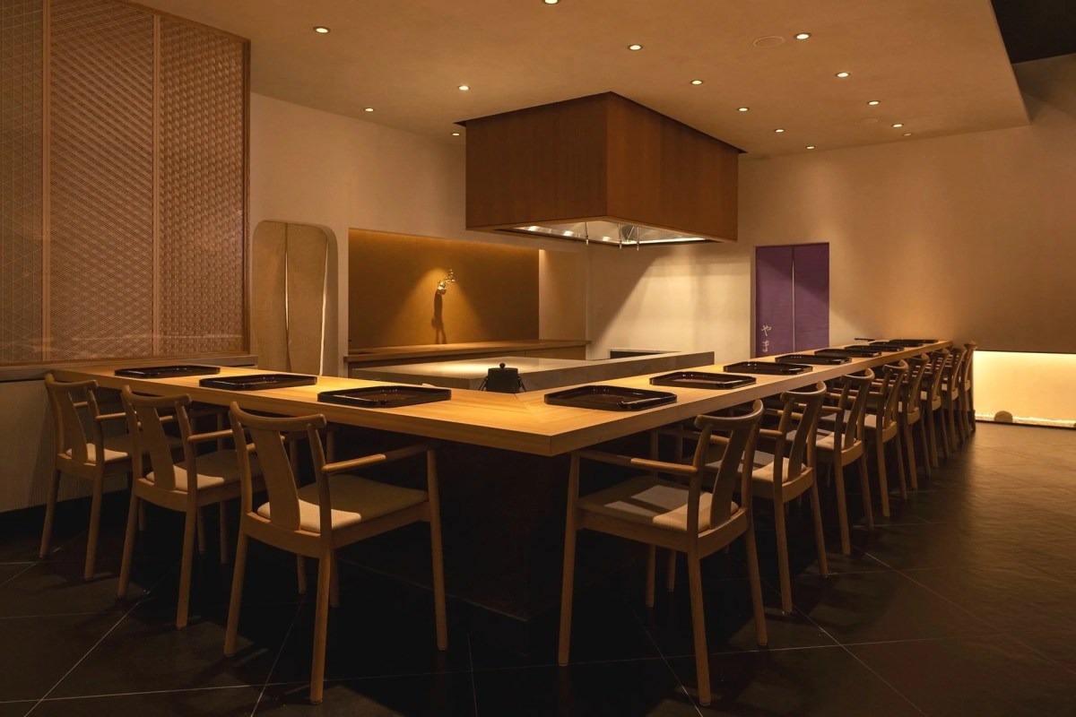 Minimalist Japanese restaurant counter with wooden chairs and small serving trays set for diners
