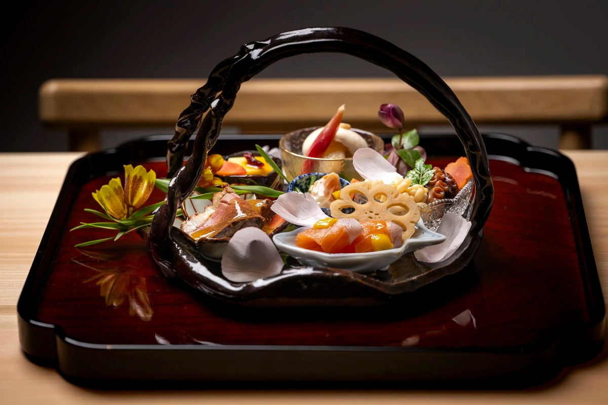 Elaborate Japanese basket-shaped dish with sashimi, lotus root, flowers and garnishes on a lacquer tray