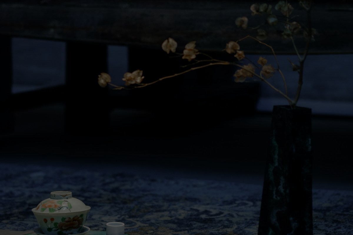 Dark, moody shot of a table setting with a decorative teacup, small cup, and a vase holding a dried branch.