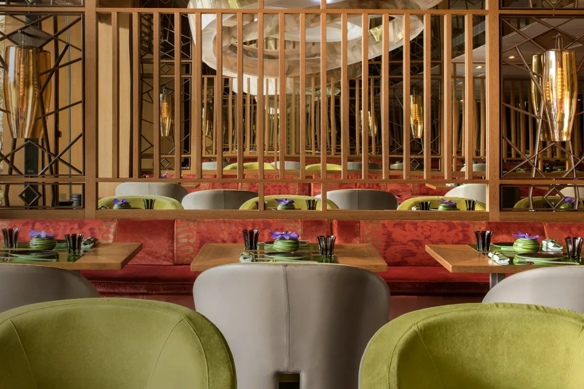 Modern Japanese restaurant dining room with green velvet chairs, red banquette seating, and wood-slat mirrored walls