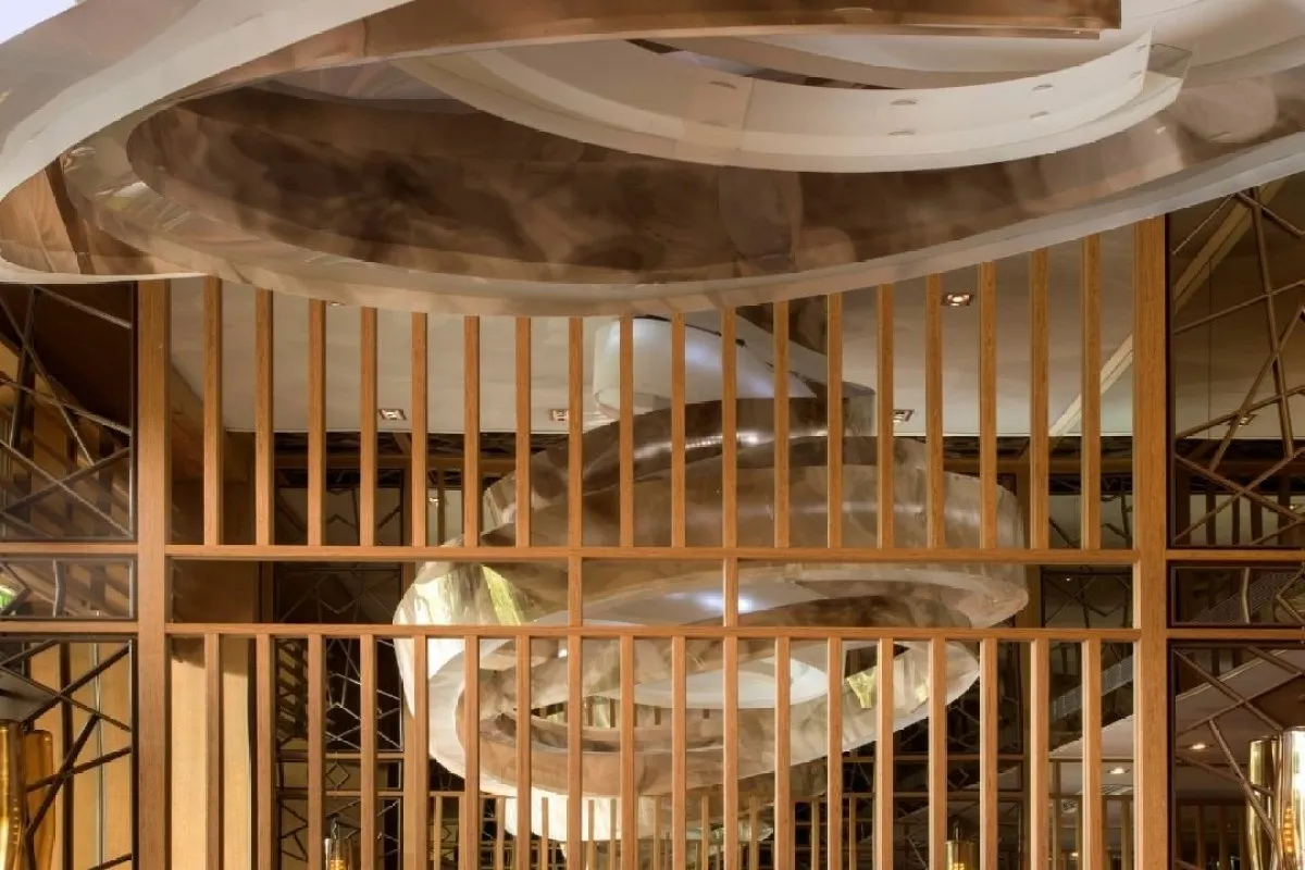 Architectural ceiling detail with wood slats and swirling metallic sculptural light fixture in restaurant interior