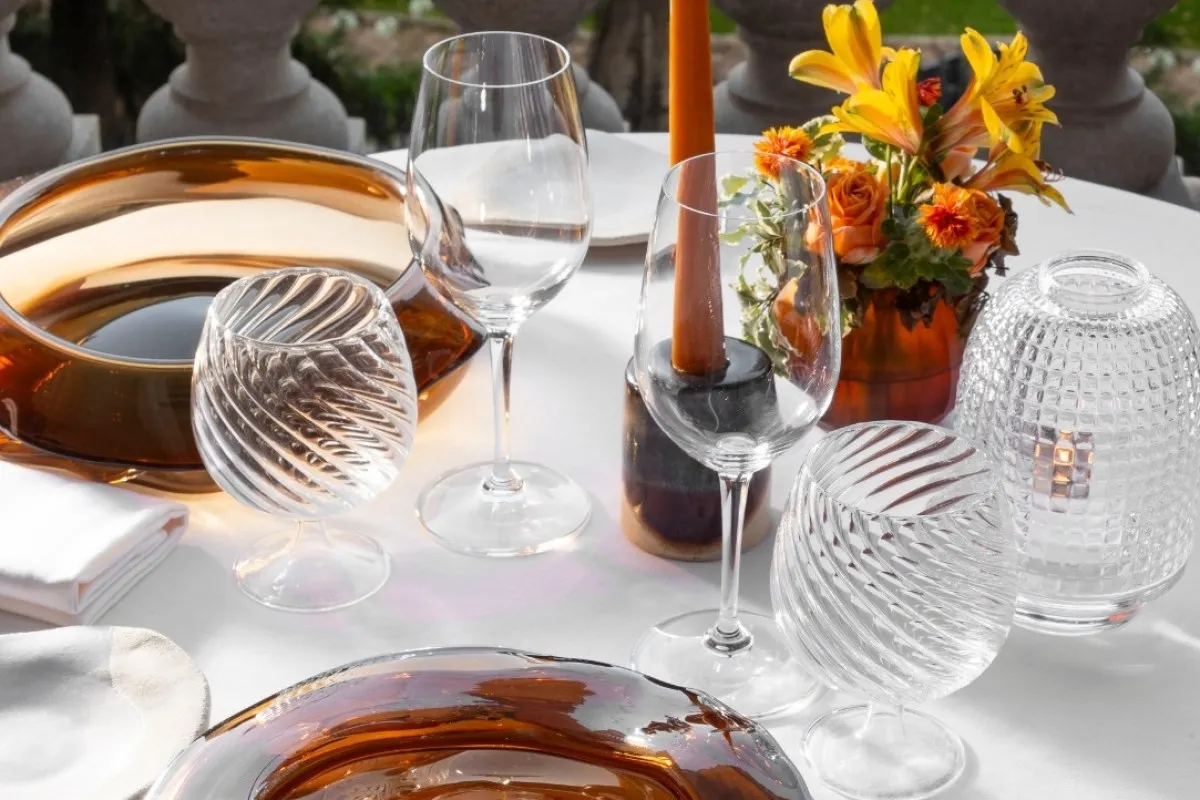 Outdoor restaurant table setting with crystal glassware, amber plates, and orange flowers on white linen