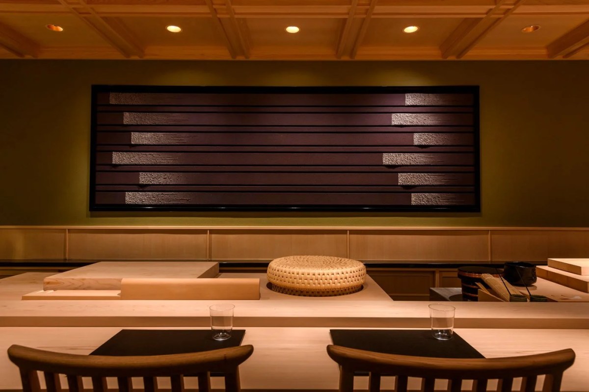 Sushi counter view with wooden bar, cushioned seat, and dark wall art