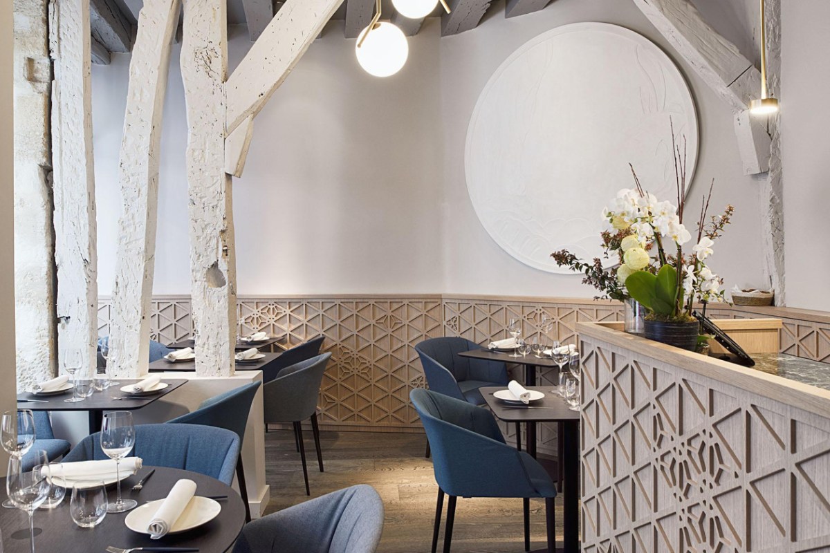 Restaurant dining room with blue chairs, white beams, and reception counter