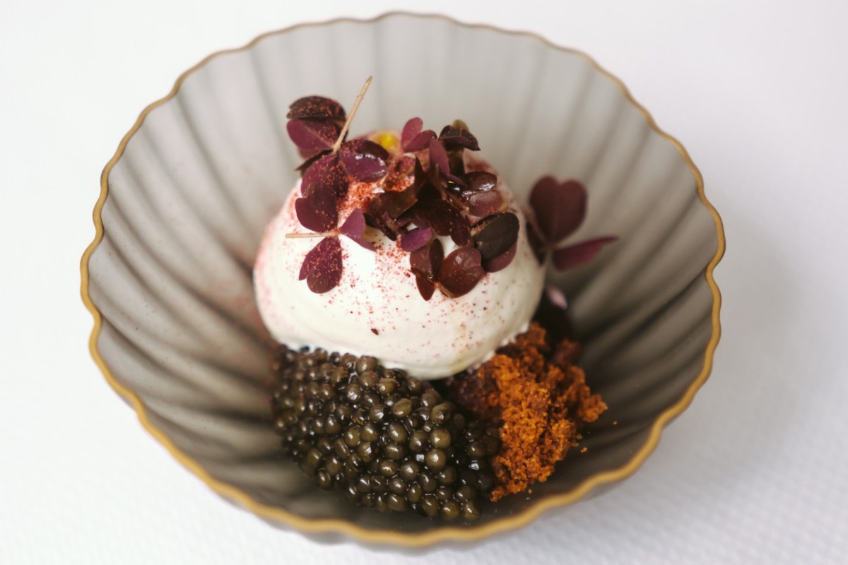 Plated dish with cream quenelle, caviar, crumble, and purple leaves in ribbed bowl