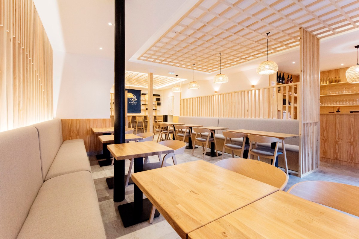 Full view of the dining room with wooden tables, bench seating, lattice ceiling, and a bar in the background