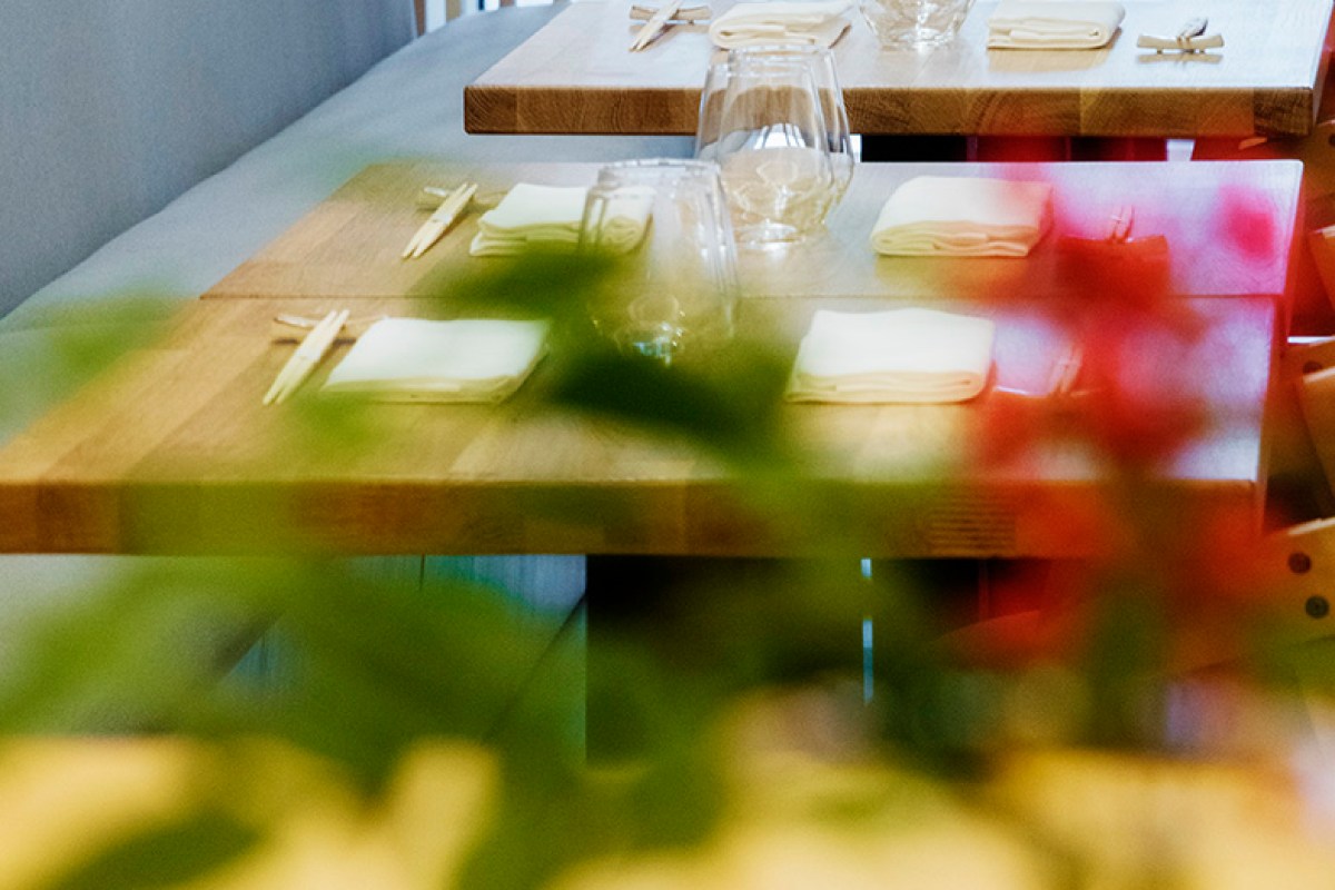 Close-up of a set table with chopsticks, folded napkins, and wine glasses, framed by blurred foliage