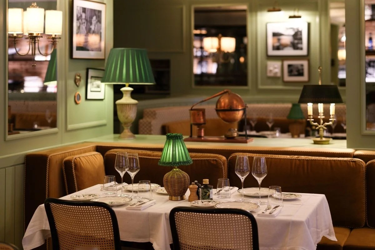 Zeffirino's dining room in Monaco with almond-green walls, velvet banquettes, cane chairs and a table set under a pleated green lamp
