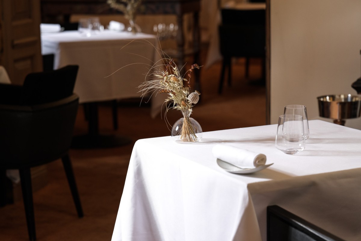 Elegant dining room with white-clothed table, dried flower vase, wine glasses in soft light