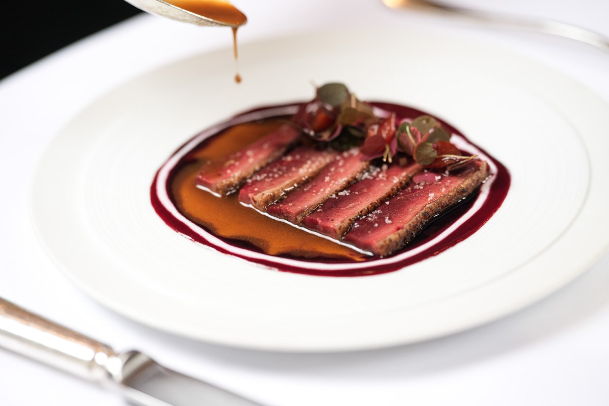 Seared tuna slices with red wine reduction sauce being poured, garnished with herbs