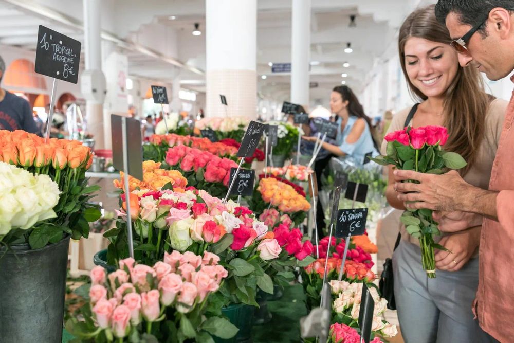 Buckets of roses at a flower stall in the Marché Forville, Cannes, with shoppers choosing a bunch