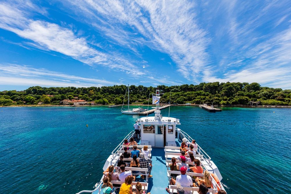 Passengers on the bow of a ferry heading across turquoise water to Île Sainte-Marguerite