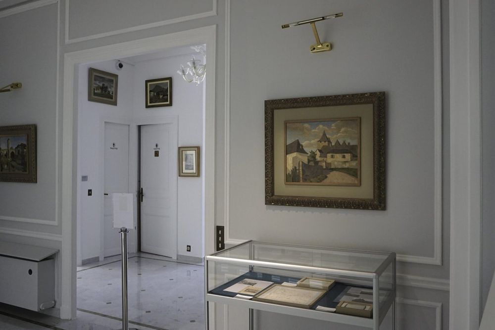 A white gallery room in the Villa les Camélias museum with framed paintings and a display case of documents