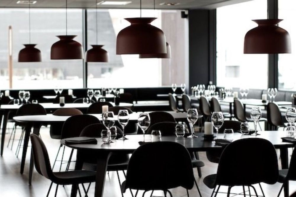 The minimalist dining room at no.2, with black chairs, laid tables and large pendant lamps by tall harbour windows