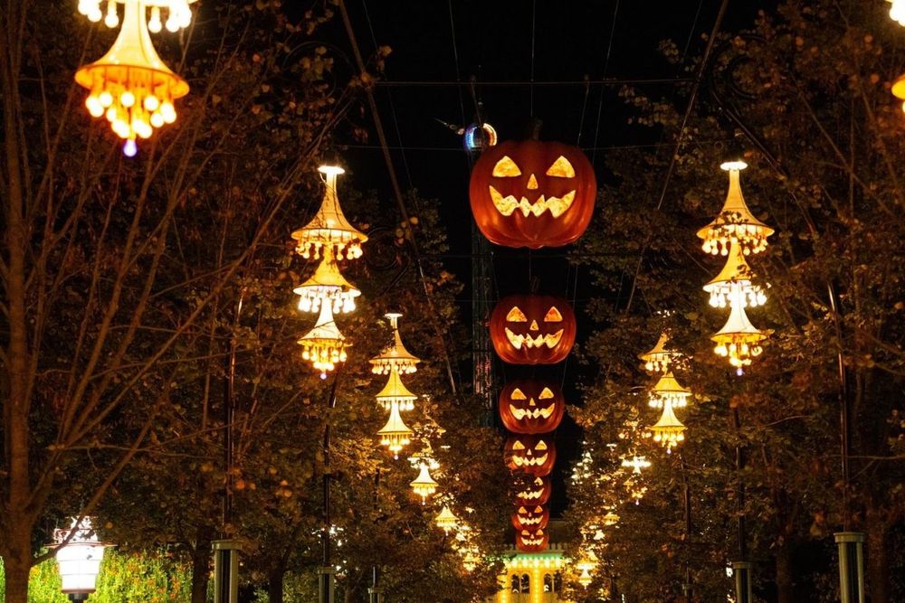 Glowing jack-o'-lantern lights and chandeliers hanging over an autumn avenue in Tivoli Gardens after dark