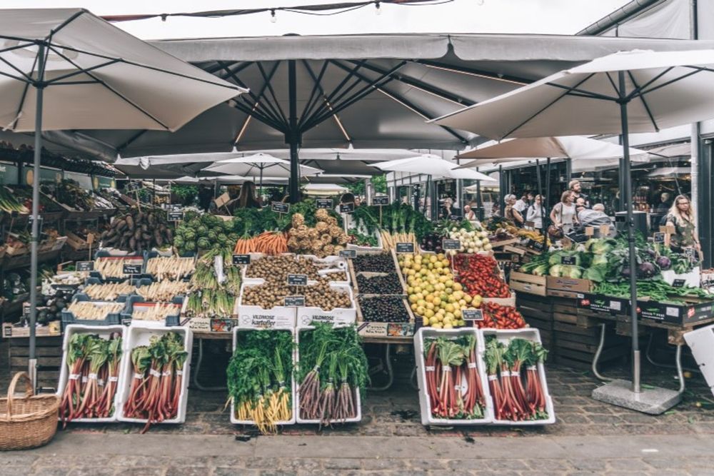 Crates of vegetables and fruit under white parasols at the outdoor stalls of Torvehallerne