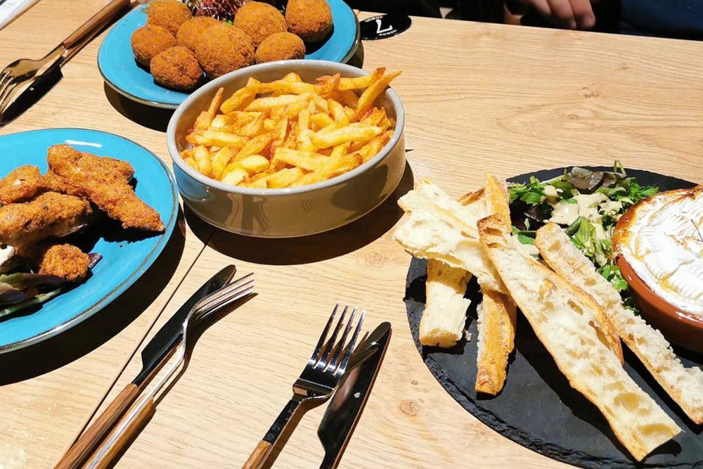 Plates of croquettes, chips and dips to share on a wooden table at La Belle Équipe