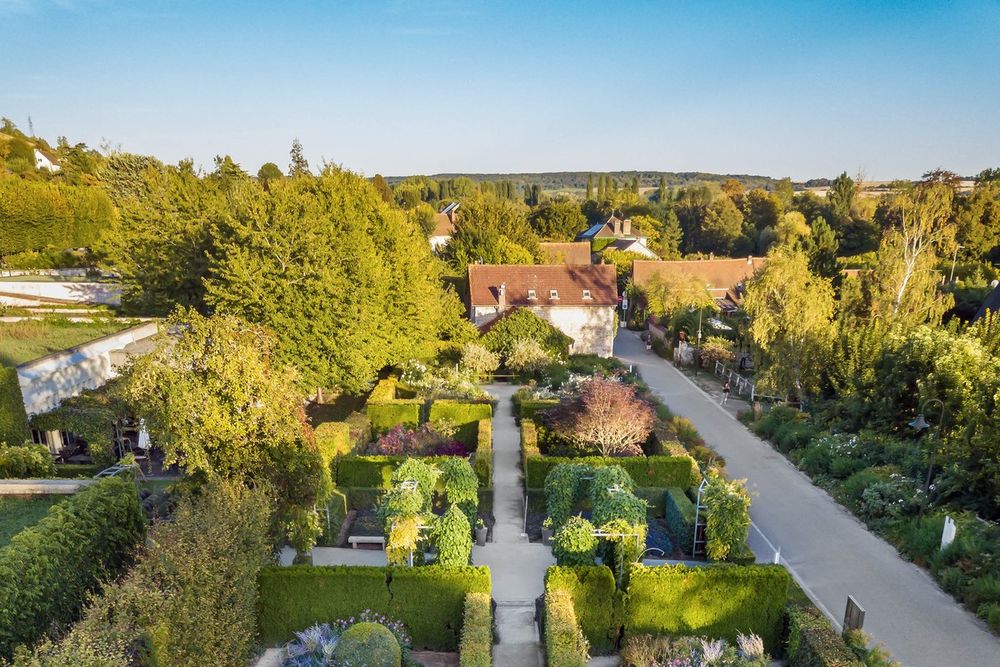 Hedged flower beds of the Musée des impressionnismes garden with Giverny's rooftops and hills beyond