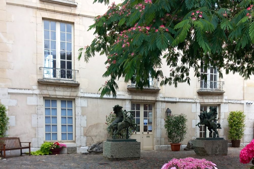 The courtyard façade of the Musée de Vernon with bronze sculptures and flowering pots