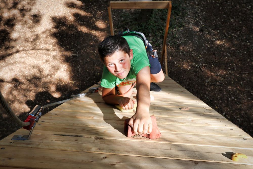 A boy pulling himself up onto a wooden platform on a tree-top course at Grimaud Aventure