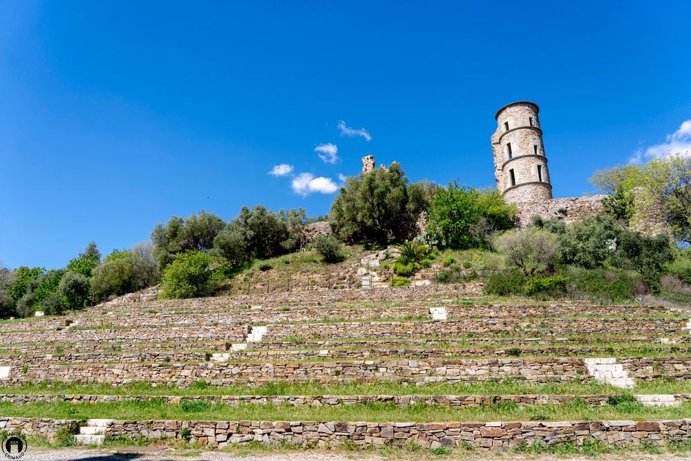 The round tower of the Château de Grimaud above grassy terraces under a blue sky