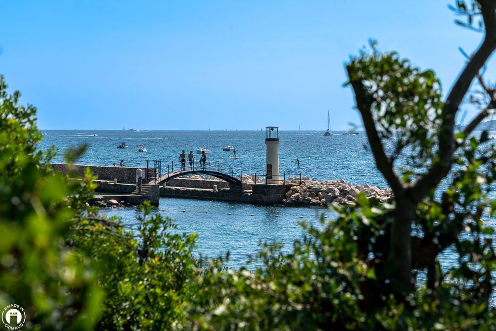The little lighthouse and arched footbridge of the Plage des Cigales seen through pine branches