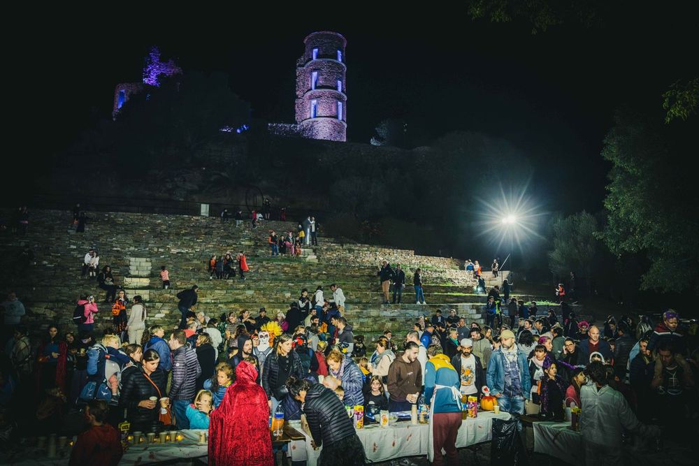 A crowd on the grassy terraces below the floodlit castle tower of Grimaud on Halloween night