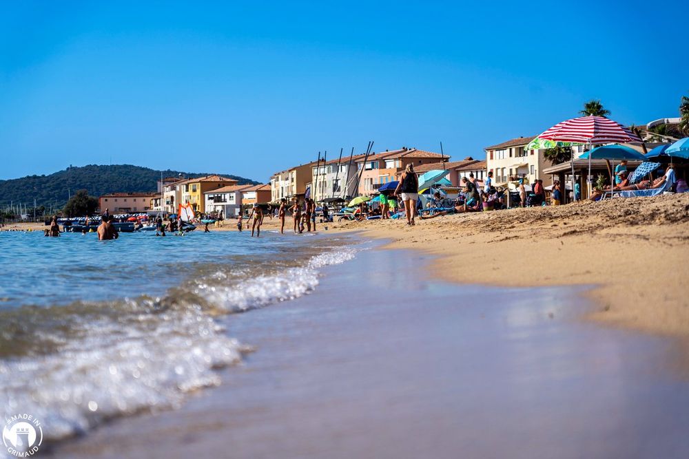 Small waves running up the sand of the Plage de Port Grimaud, with beach umbrellas and houses beyond