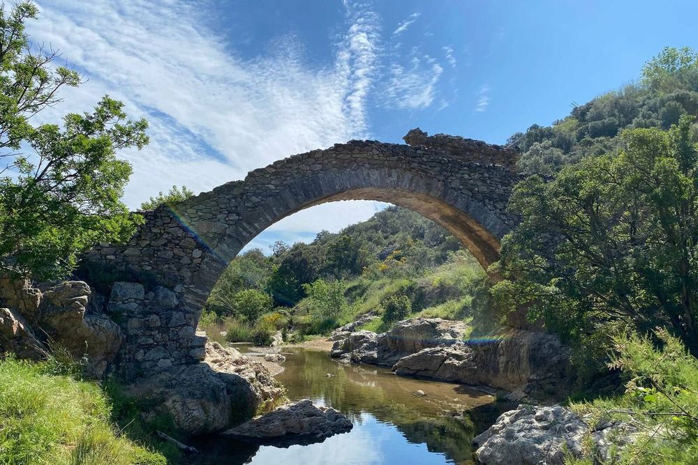The arch of the Pont des Fées reflected in a pool of the La Garde stream