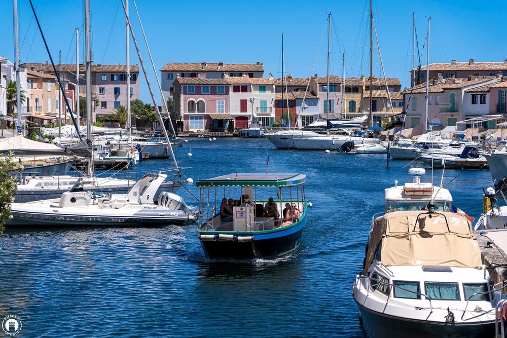 A small canopied boat with passengers gliding between moored yachts in Port Grimaud