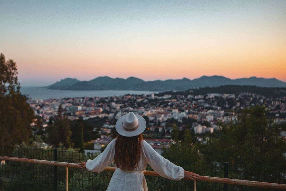 A walker at a railing on the heights of Le Cannet as the sun sets over the bay of Cannes and the Estérel
