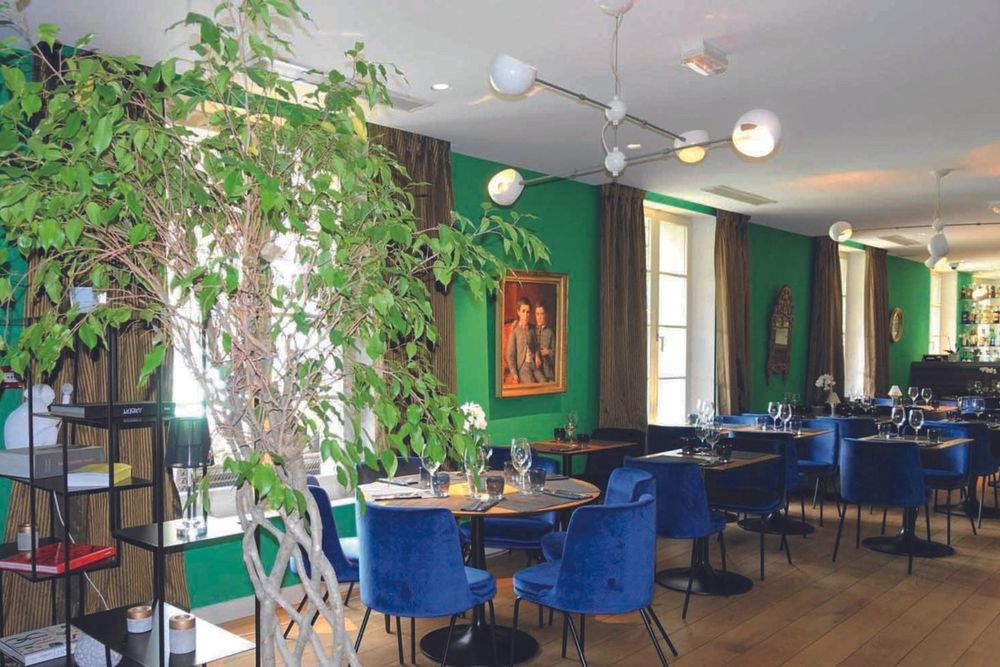 The green-walled dining room of Le Bistrot des Anges, with blue velvet chairs and an olive tree
