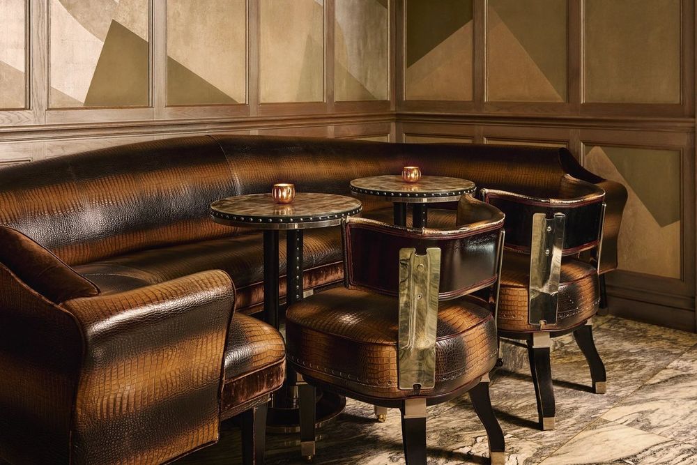 A curved leather banquette and small round tables in a corner of the Connaught Bar