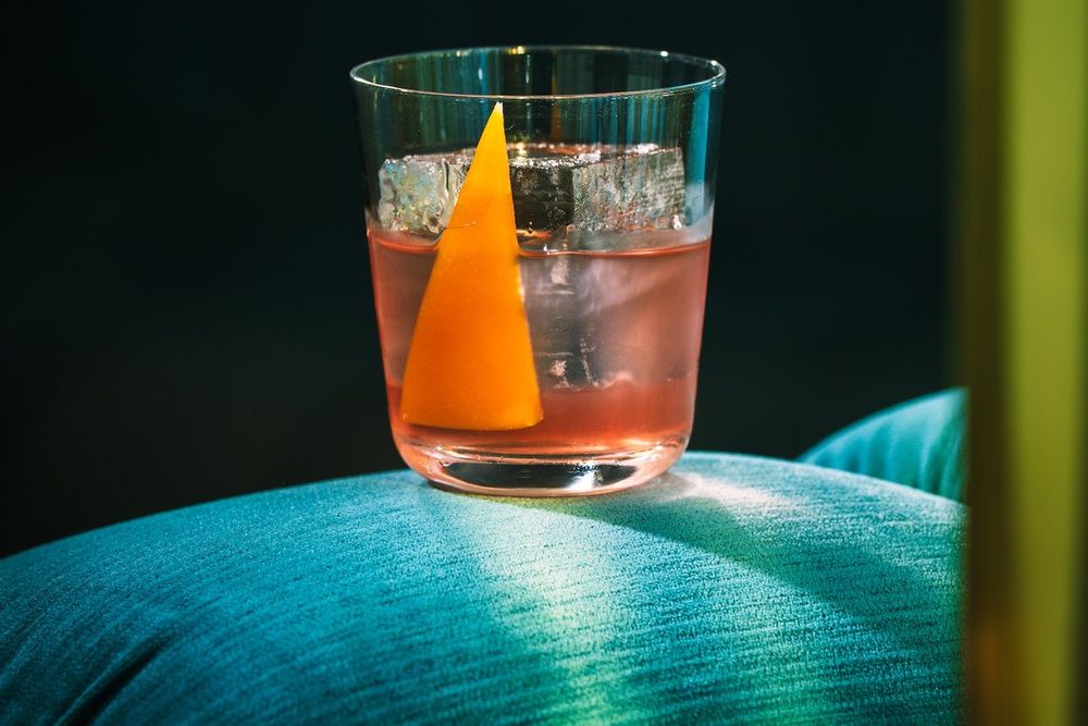 A Lyaness cocktail with an orange garnish on a blue velvet seat