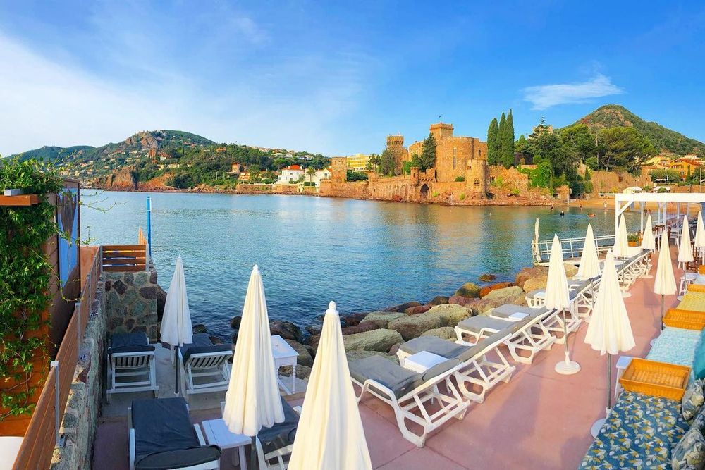 White parasols and loungers on Dolce Farniente's deck in the port of La Napoule, the château across the bay