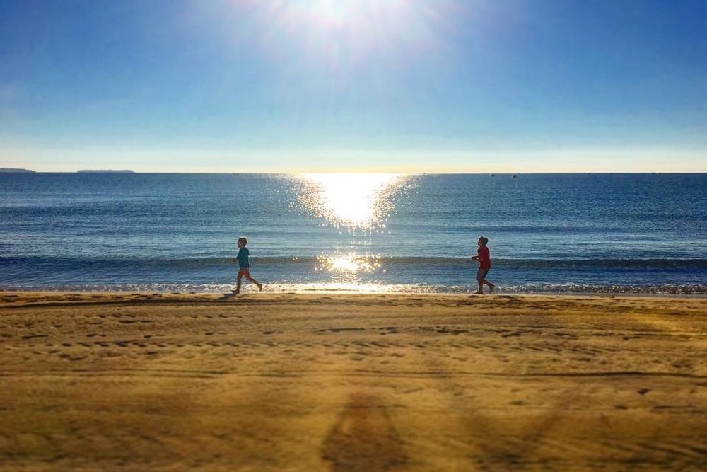 The sun low over the sea at Plage de Robinson, Mandelieu, with two walkers on the sand