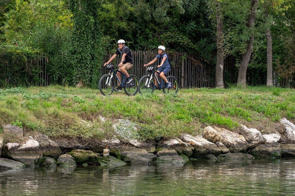 Two cyclists riding along the green banks of the Siagne beside the riverside rocks