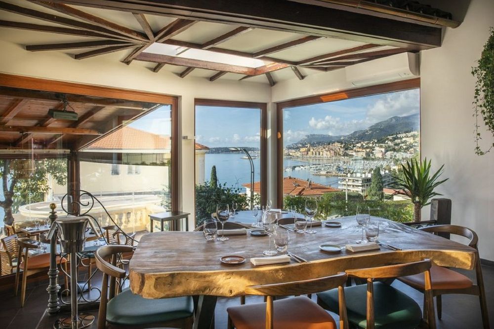 The wood-beamed dining room of Casa Fuego with a picture window over Menton's harbour and old town